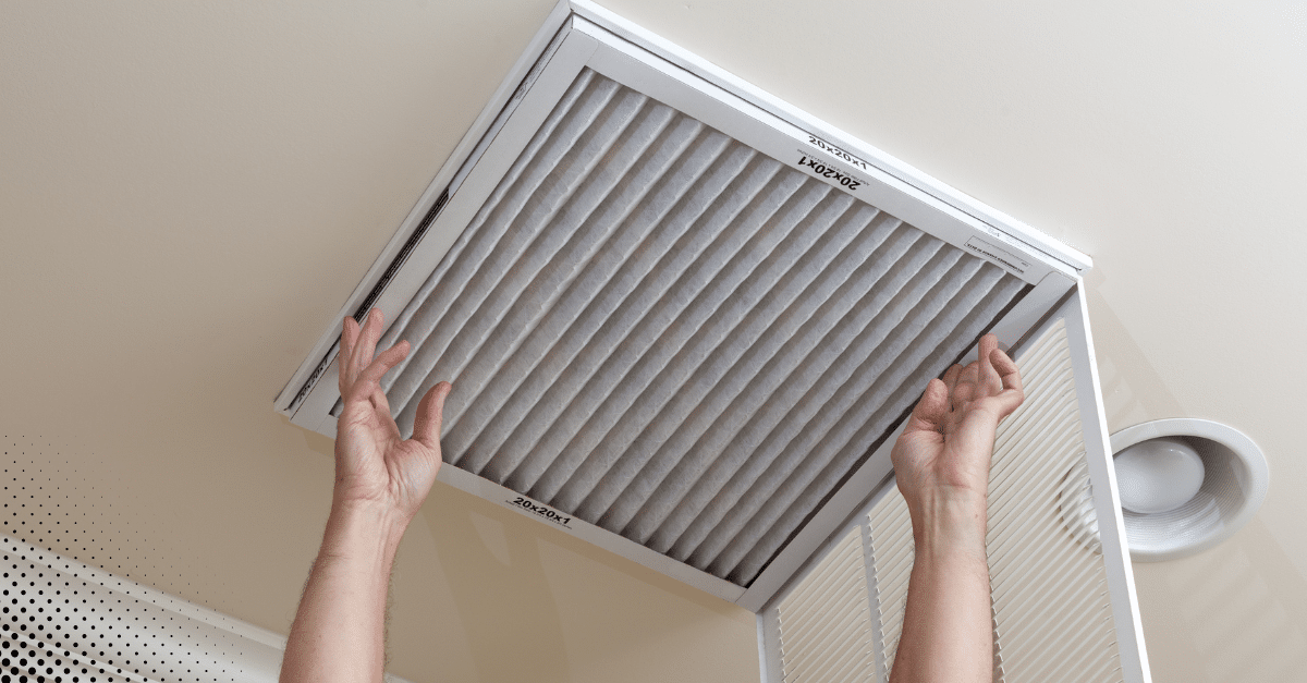Hands changing the air filter in an HVAC ceiling vent.