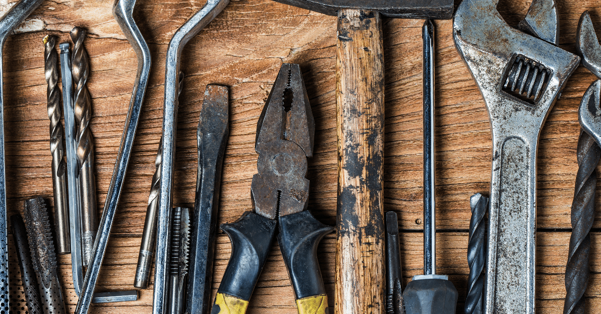 Tools arranged on a wooden surface, including pliers, wrenches, drill bits, and a hammer, representing essential equipment for home maintenance and inspections in Florida's climate.